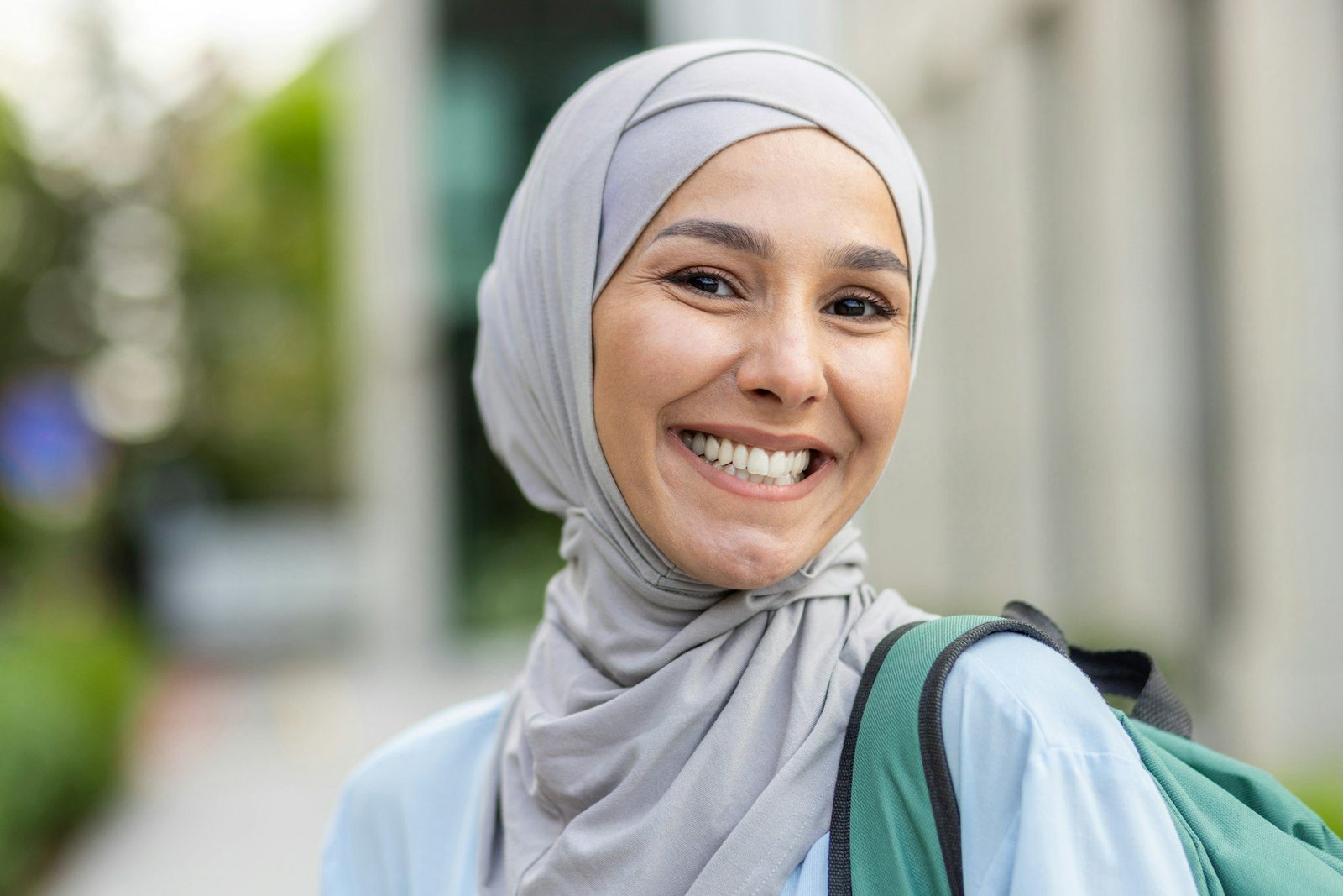 Close-up portrait of Muslim female student in hijab, woman with backpack behind her back smiling