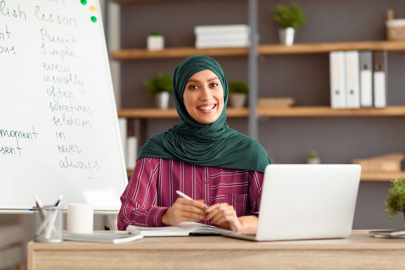 Islamic teacher in headscarf sitting at desk looking at camera